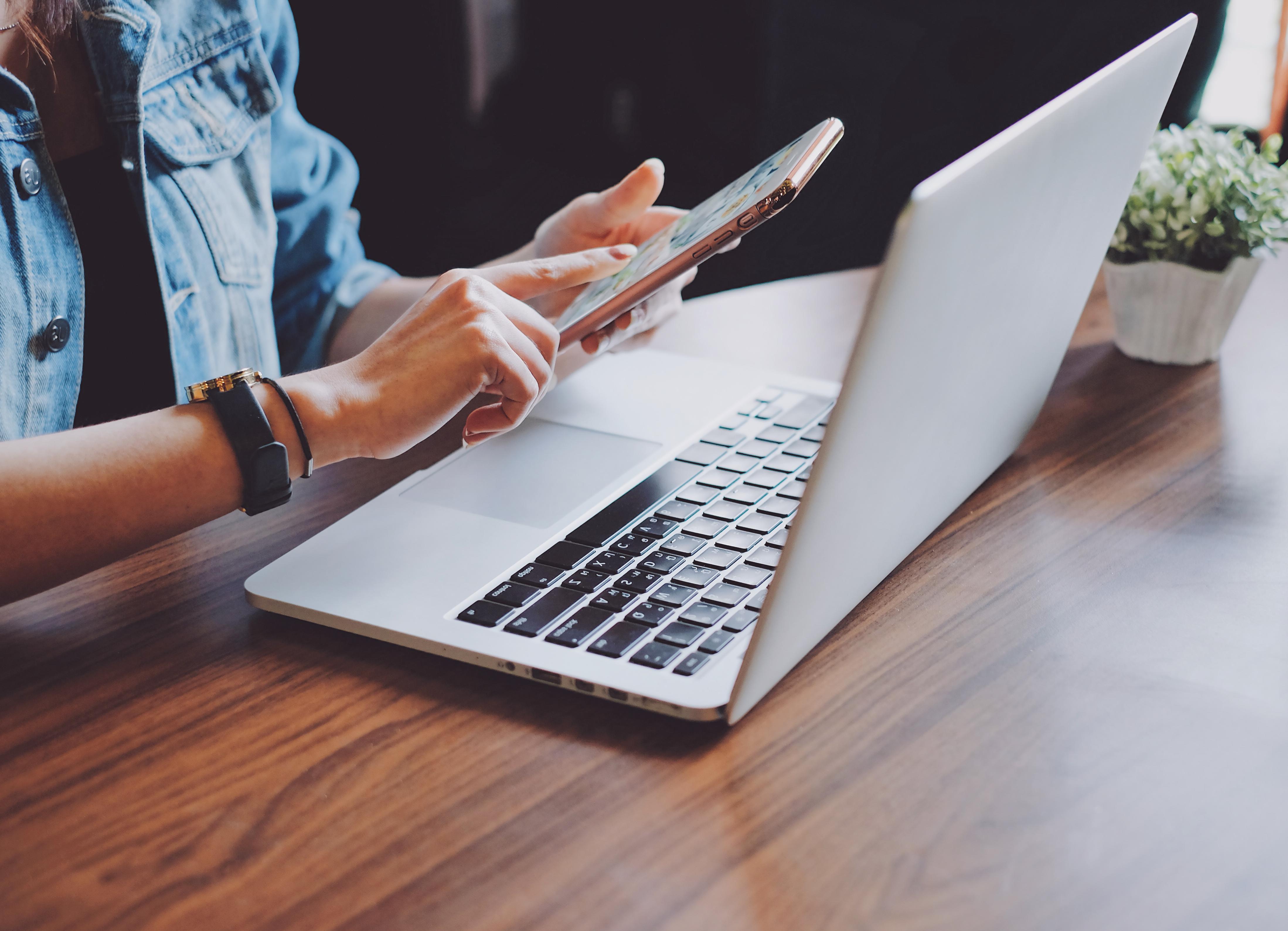 Young hipster woman using smartphone and laptop in office or